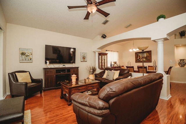 living room featuring wood-type flooring, ceiling fan with notable chandelier, ornate columns, and vaulted ceiling