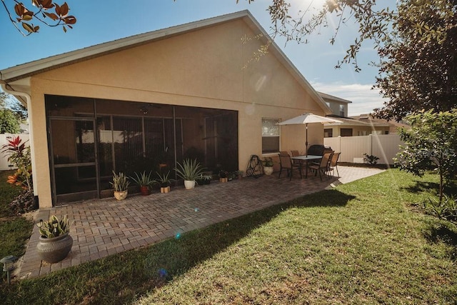 back of property featuring a sunroom, a patio area, and a lawn