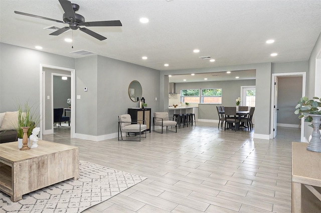 living room featuring a textured ceiling, light hardwood / wood-style floors, and ceiling fan