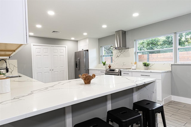 kitchen featuring white cabinetry, a breakfast bar, wall chimney range hood, and appliances with stainless steel finishes