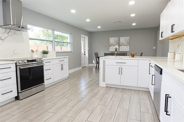 kitchen with kitchen peninsula, light wood-type flooring, stainless steel appliances, and wall chimney exhaust hood