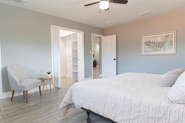 bedroom with a walk in closet, a textured ceiling, ceiling fan, light hardwood / wood-style flooring, and a closet