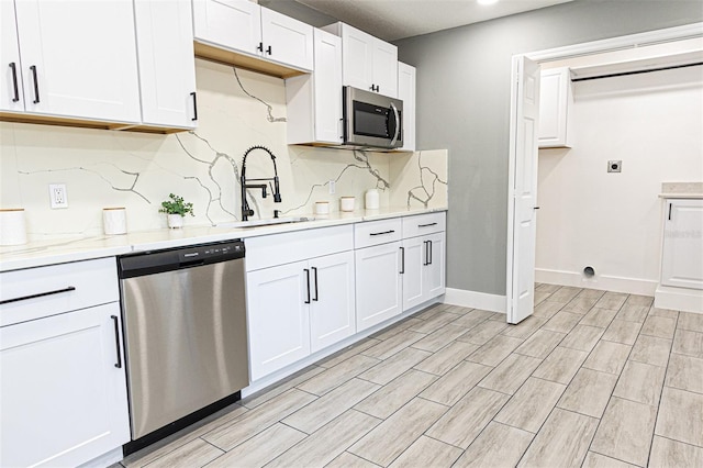 kitchen featuring stainless steel appliances, white cabinetry, light stone countertops, and sink