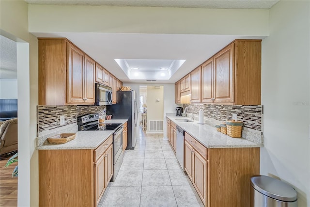 kitchen featuring light stone countertops, appliances with stainless steel finishes, backsplash, a tray ceiling, and sink