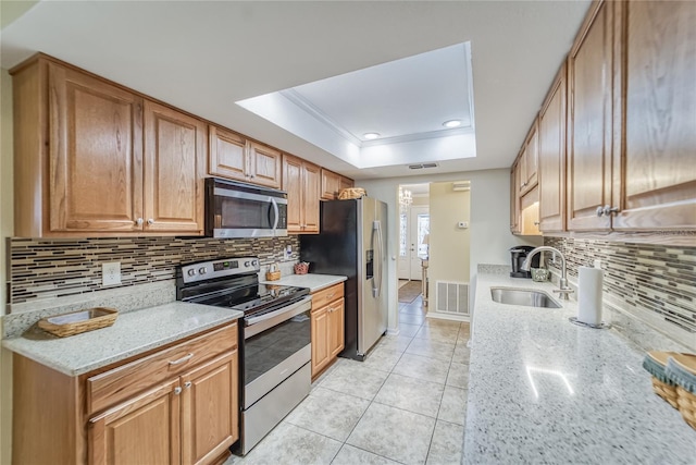 kitchen with a tray ceiling, light stone counters, sink, and stainless steel appliances