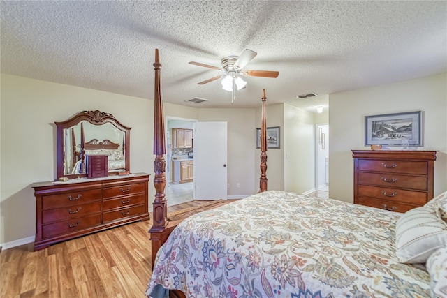 bedroom featuring ceiling fan, ensuite bathroom, light hardwood / wood-style floors, and a textured ceiling