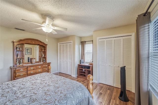 bedroom featuring ceiling fan, wood-type flooring, a textured ceiling, and multiple closets