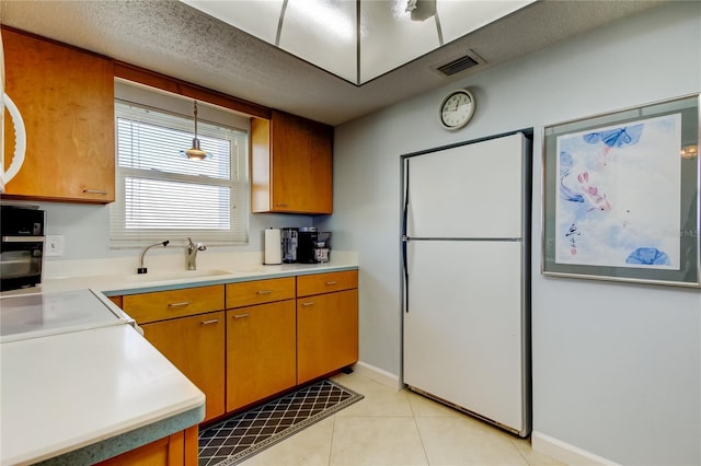 kitchen featuring sink, light tile patterned floors, a textured ceiling, decorative light fixtures, and white fridge