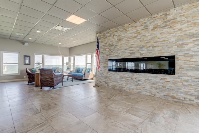 living room with a stone fireplace, a paneled ceiling, and light tile patterned flooring