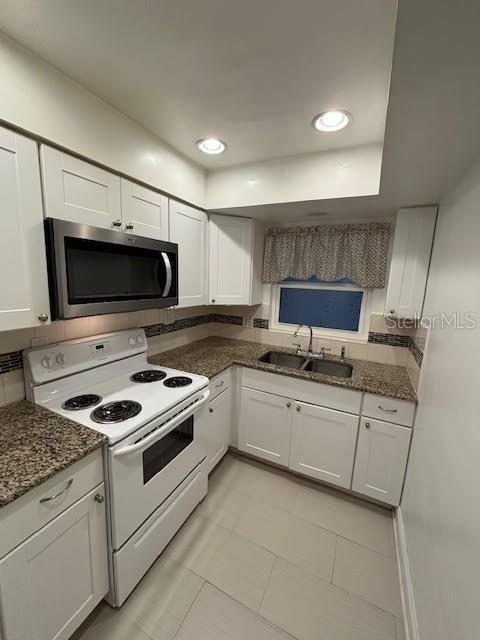 kitchen featuring white electric stove, white cabinets, dark stone counters, stainless steel microwave, and a sink