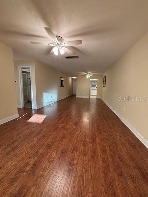 unfurnished living room featuring dark wood-type flooring, ceiling fan, a textured ceiling, and baseboards