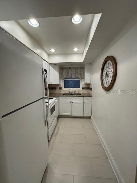 kitchen featuring dark countertops, freestanding refrigerator, white cabinetry, white range with electric cooktop, and recessed lighting