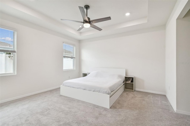 bedroom featuring a raised ceiling, ceiling fan, light colored carpet, and multiple windows