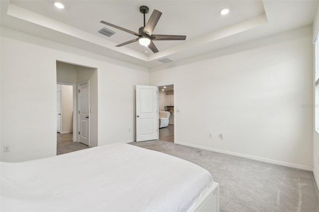 carpeted bedroom with a raised ceiling and ceiling fan