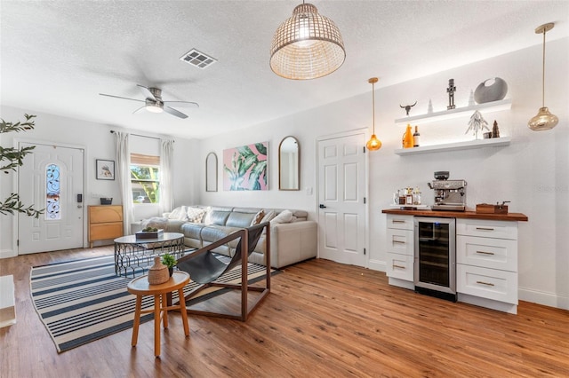 living room with a textured ceiling, light wood-type flooring, wine cooler, and ceiling fan