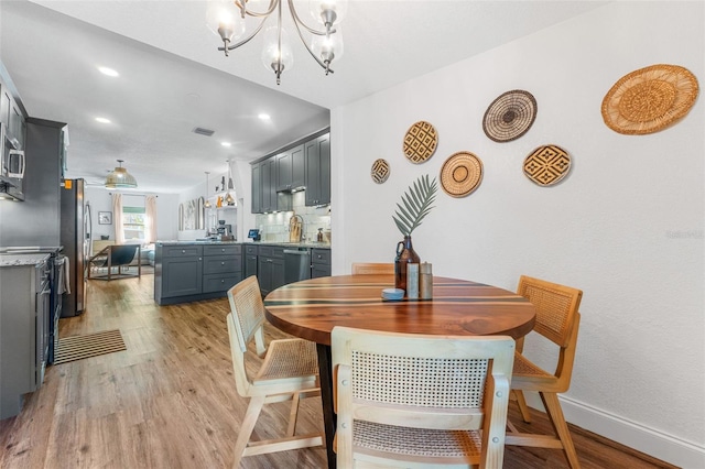 dining area with light wood-type flooring, sink, and an inviting chandelier