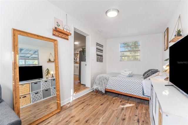 bedroom with multiple windows, light hardwood / wood-style flooring, and white refrigerator