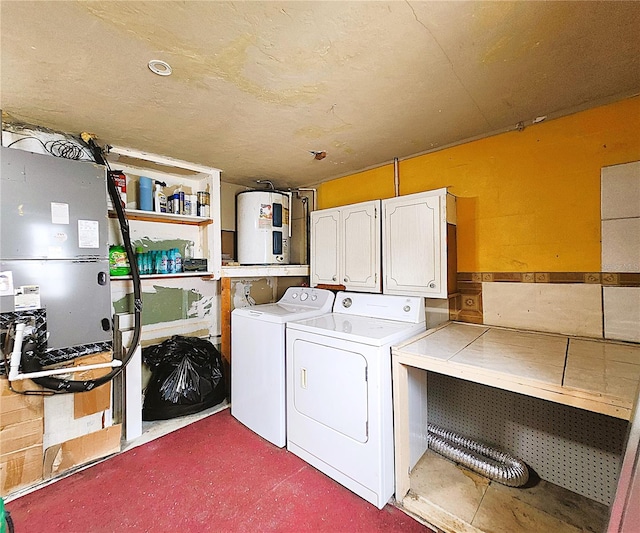 clothes washing area featuring electric water heater, washer and clothes dryer, and cabinets