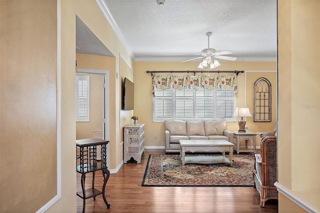 living area featuring hardwood / wood-style flooring, ceiling fan, ornamental molding, and a textured ceiling