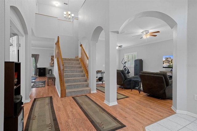 exercise room with ornamental molding, ceiling fan with notable chandelier, and light wood-type flooring