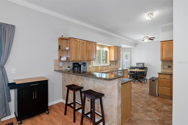 kitchen with dark stone counters, ceiling fan, ornamental molding, kitchen peninsula, and a breakfast bar area