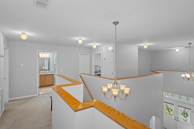 hall featuring french doors, light carpet, and an inviting chandelier