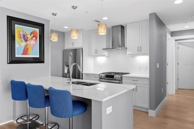 kitchen with stainless steel appliances, wall chimney range hood, pendant lighting, light hardwood / wood-style floors, and white cabinetry