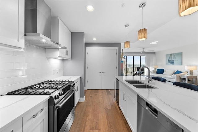 kitchen with wall chimney range hood, sink, appliances with stainless steel finishes, light hardwood / wood-style floors, and white cabinetry