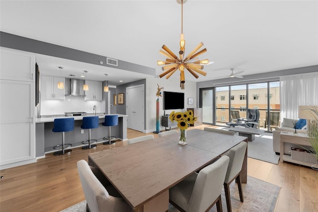 dining space with ceiling fan with notable chandelier, light hardwood / wood-style flooring, and sink