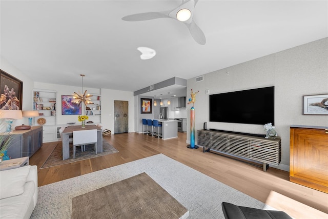 living room with ceiling fan, built in features, and wood-type flooring