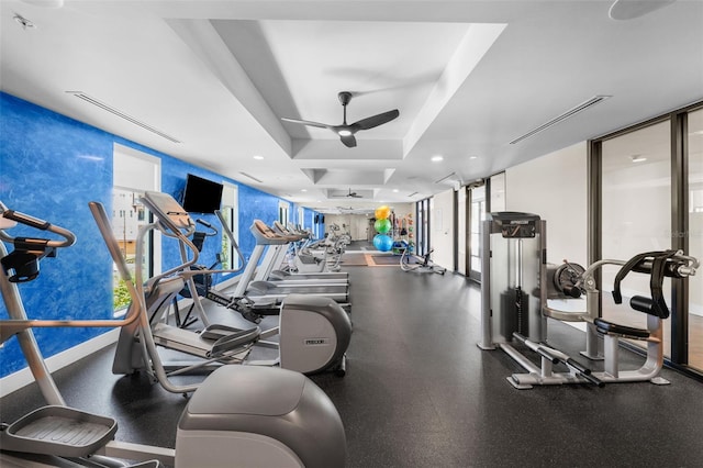 exercise room with floor to ceiling windows, a raised ceiling, and ceiling fan