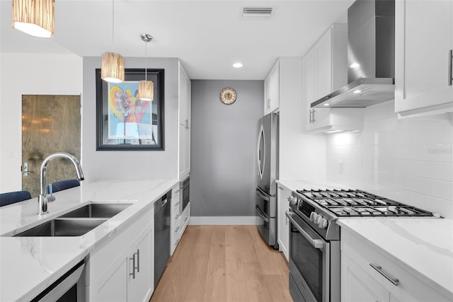 kitchen featuring stainless steel appliances, wall chimney range hood, pendant lighting, light hardwood / wood-style flooring, and white cabinets