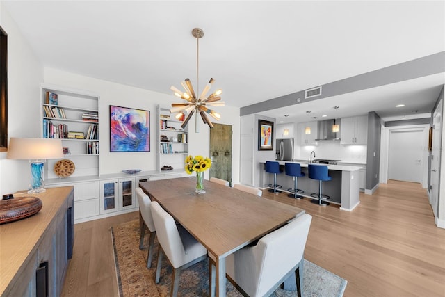 dining space with built in features, light hardwood / wood-style floors, and a notable chandelier