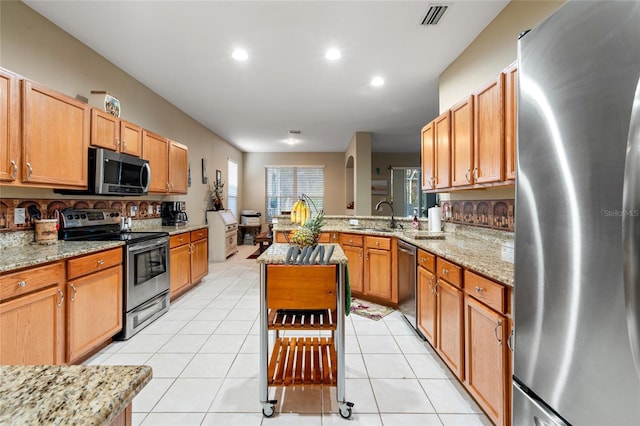 kitchen with sink, light stone counters, kitchen peninsula, light tile patterned flooring, and appliances with stainless steel finishes