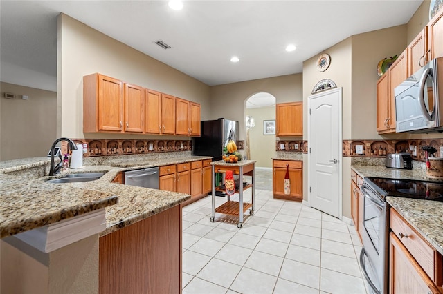 kitchen with backsplash, light stone counters, sink, and appliances with stainless steel finishes