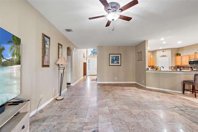 unfurnished living room featuring ceiling fan and a textured ceiling