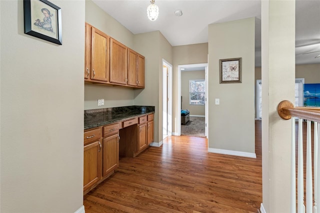 kitchen with built in desk, dark stone counters, and dark wood-type flooring