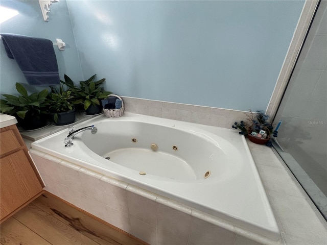 bathroom featuring vanity, a relaxing tiled tub, and wood-type flooring