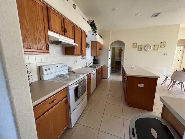 kitchen with light tile patterned floors, white appliances, tasteful backsplash, and an island with sink