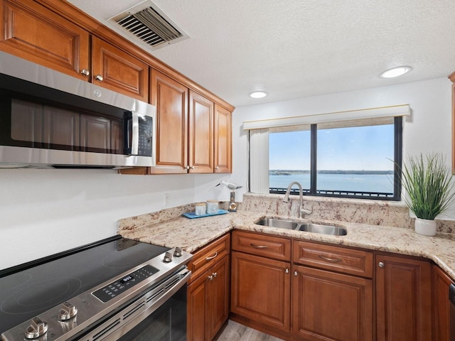 kitchen with sink, stainless steel appliances, light stone countertops, a textured ceiling, and a water view