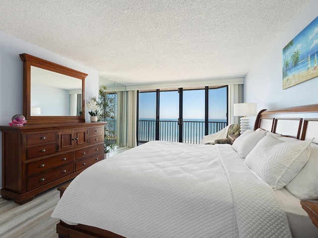 bedroom with a water view, access to exterior, light hardwood / wood-style floors, and a textured ceiling