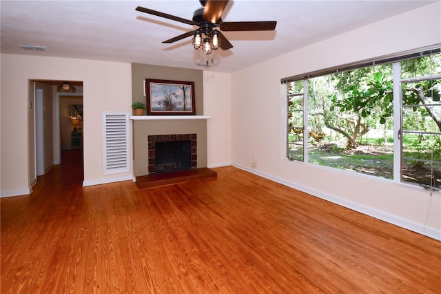 unfurnished living room featuring wood-type flooring, ceiling fan, and a tiled fireplace