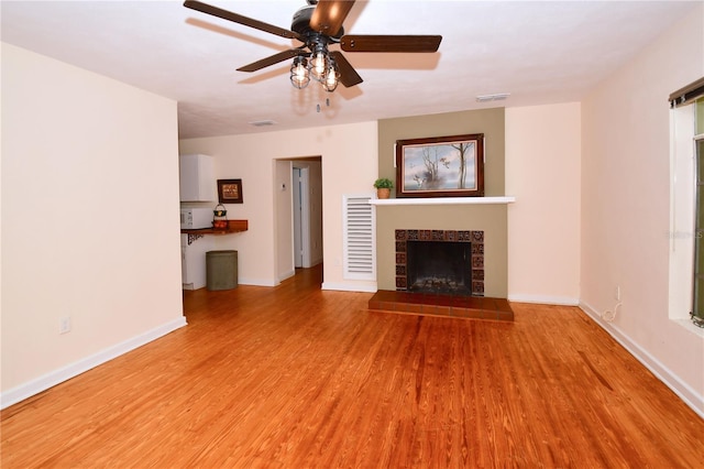 unfurnished living room featuring light wood-type flooring, ceiling fan, and a tiled fireplace