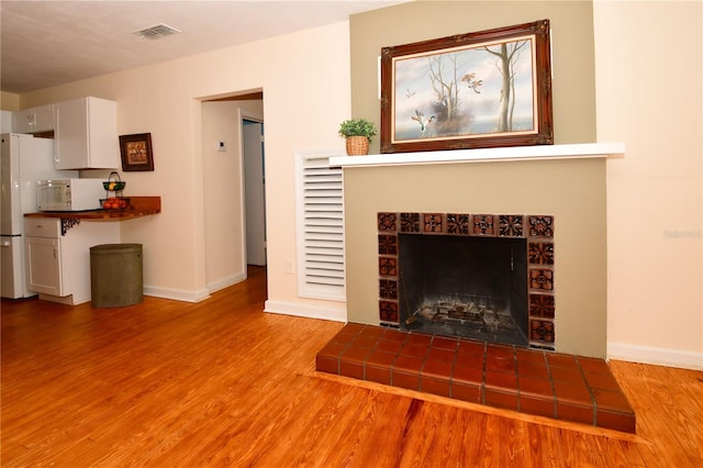 unfurnished living room with a tiled fireplace and light hardwood / wood-style flooring