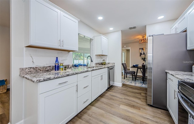 kitchen with light stone counters, stainless steel appliances, sink, light hardwood / wood-style flooring, and white cabinets