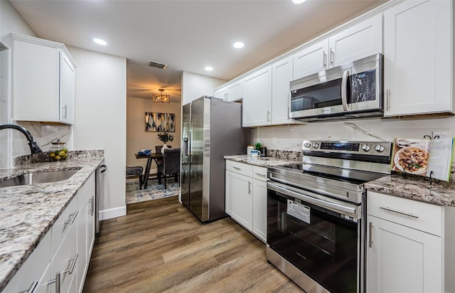 kitchen featuring white cabinets, sink, hardwood / wood-style flooring, light stone counters, and stainless steel appliances