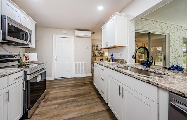 kitchen with light stone counters, stainless steel appliances, a wall mounted AC, sink, and white cabinets