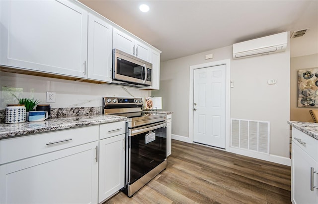 kitchen featuring white cabinets, light hardwood / wood-style flooring, light stone countertops, appliances with stainless steel finishes, and a wall mounted AC