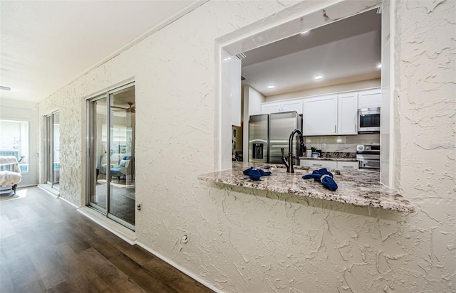 kitchen featuring white cabinets, decorative backsplash, light stone counters, appliances with stainless steel finishes, and dark hardwood / wood-style flooring