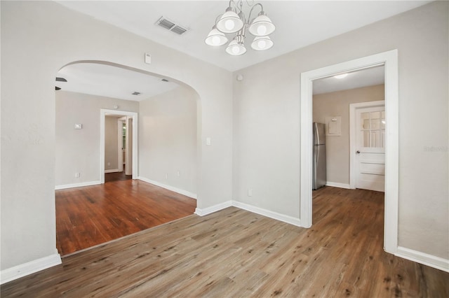 spare room with wood-type flooring and an inviting chandelier